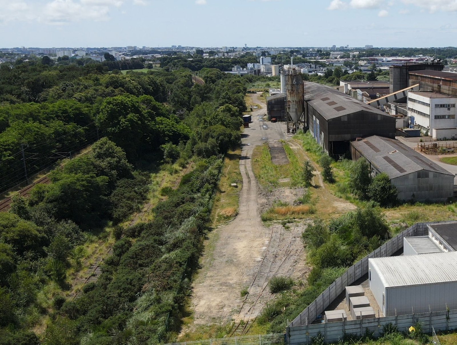 Vue aérienne d’une friche industrielle bordée de boisements, avant le projet