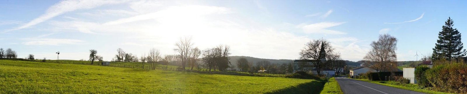 Panorama d’un bourg en bord de route avec prairie au premier plan, état initial