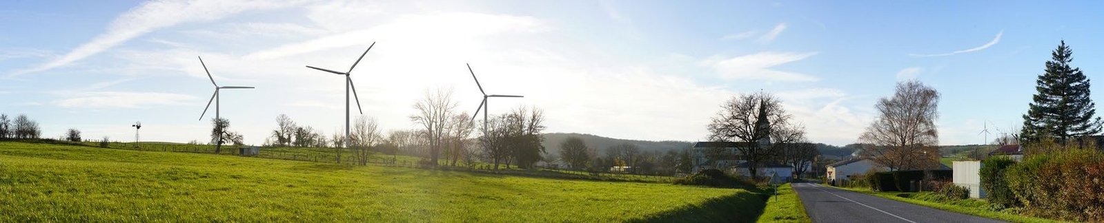 Photomontage réaliste de trois éoliennes derrière les arbres d’un bourg