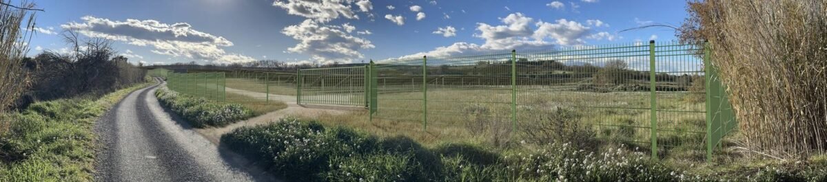 Photomontage d’une clôture et d’un portail de centrale photovoltaïque le long du chemin rural
