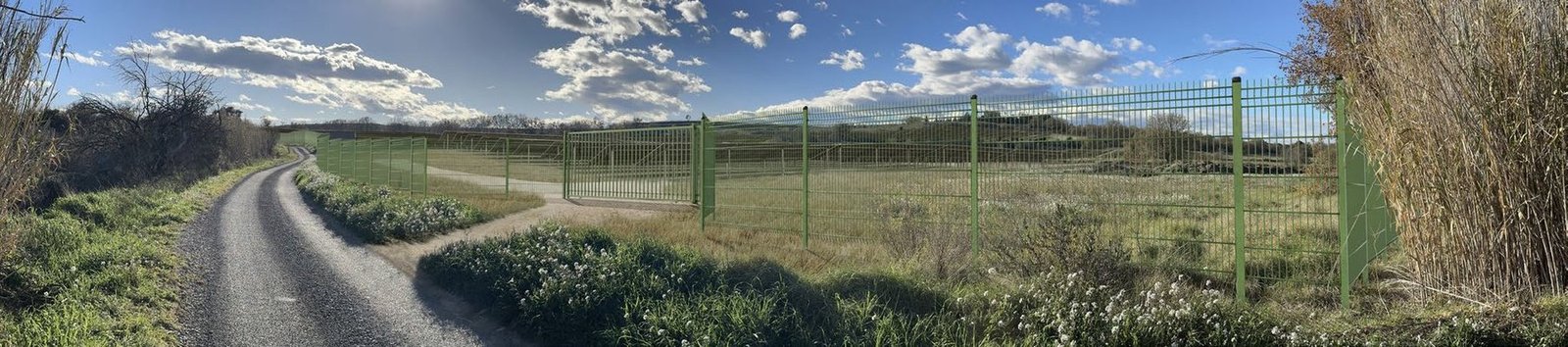Photomontage d’une clôture et d’un portail de centrale photovoltaïque le long du chemin rural